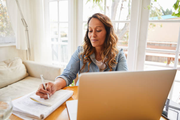 istock Mature woman writing notes and working on a laptop at home 1216764846