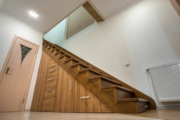 istock Modern architecture interior with luxury hallway with glossy wooden stairs in multi-storey house. Custom built pullout cabinets on glides in slots under stairs. Use of space for storage. 1216767788
