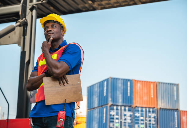istock Black foreman worker working control the crane and forklift at Container cargo harbor to loading containers. African dock male staff for Logistics import export shipping concept. 1216775901