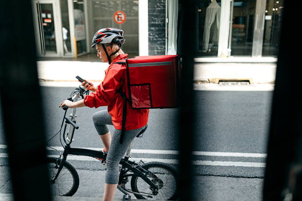 istock Food delivery woman looking for address using mobile phone on bicycle 1216776232