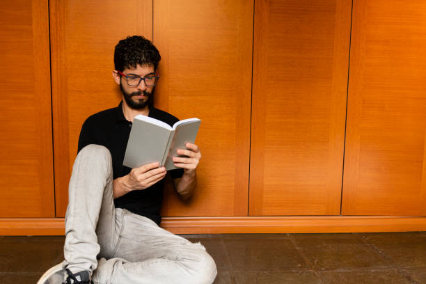 istock Latin looking to distract himself by reading book during quarantine in his room 1216777858