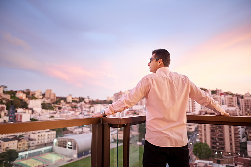 Rear view shot of a businessman standing in office balcony and looking at the city view