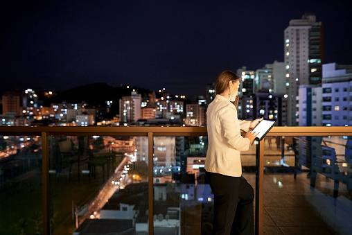 Rear view shot of a businesswoman standing in office balcony using digital tablet