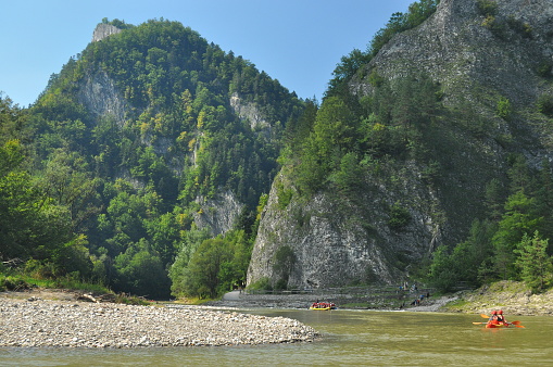 Rafting on the Dunajec River in the Pieniny National Park on wooden folding shuttles tied with a rope. Rafters paddling on a rapid stream with a rocky bottom and strong river current.