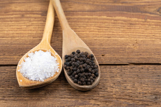 coarse crystal salt and whole black peppercorns on wooden spoons on a rustic wooden background - salt crystal spoon food imagens e fotografias de stock