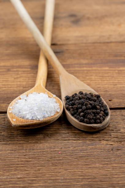 sal de cristal gruesa y granos de pimienta negros enteros en cucharas de madera sobre un fondo rústico de madera - salt crystal spoon food fotografías e imágenes de stock