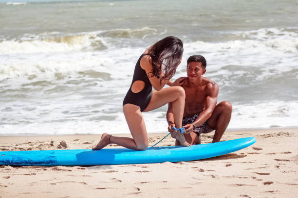 istock Young handsome man sitting beside longboard,teaching basic pattern of surfing to beautiful lady,on the beach 1216781155