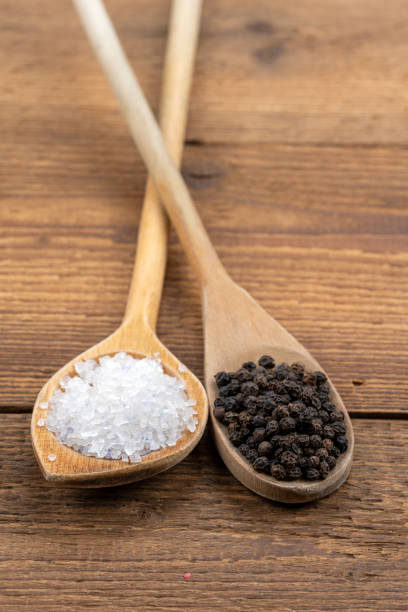 coarse crystal salt and whole black peppercorns on wooden spoons on a rustic wooden background - salt crystal spoon food imagens e fotografias de stock