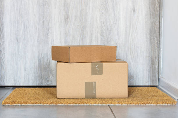 istock Parcel in cardboard box left on near door on rug. 1216783919