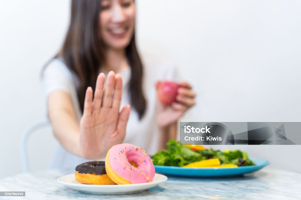Asian young woman refuse junk food while choose to eat healthy salad and fruit juice for her healthy. Girl take care of herself by having high nutrition food every day. Good food for healthy concept. Diabetes Stock Photo