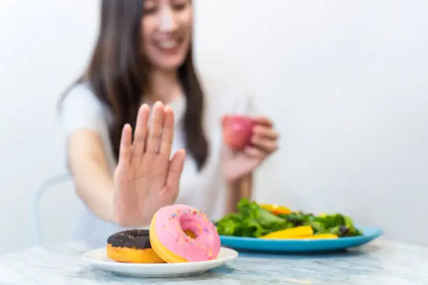 Asian young woman refuse junk food while choose to eat healthy salad and fruit juice for her healthy. Girl take care of herself by having high nutrition food every day. Good food for healthy concept.