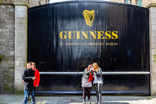 Dublin, Ireland - April 22, 2016: Street view of people in front of the historic old factory building wooden gate entrance at Guinness St. James´s Gate Brewery in Dublin Ireland April 22, 2016. Company sign on the gate.
