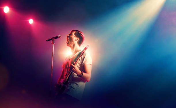 Singer with microphone and guitar performing on stage Musical performance. Young male rock singer performing on stage and playing the guitar popular music concert stock pictures, royalty-free photos & images