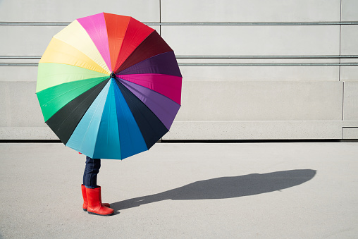 Standing girl with multicolored umbrella in front of a concrete wall