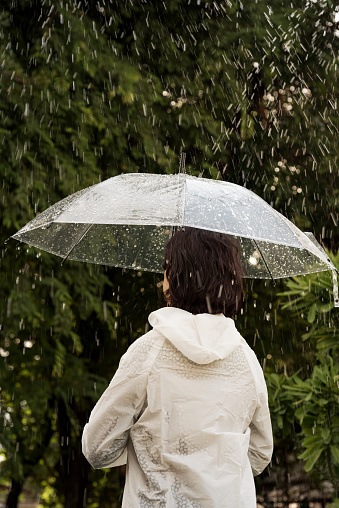 In raining day woman open umbrella stand in garden feel happyand have warmth,romantic feeling.