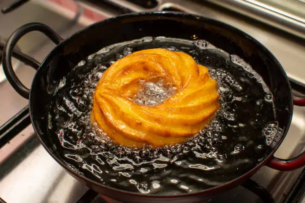 Fritters made from cream-puff dough, austrian desert speciality cooking in oil in metal pan on stove