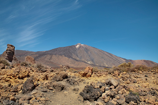 Mount Teide surrounded by the rocky volcanic and unusual landscape with Roque Cinchado on the left, situated in the popular travel destination Teide National Park, in Tenerife, Canary Islands, Spain.