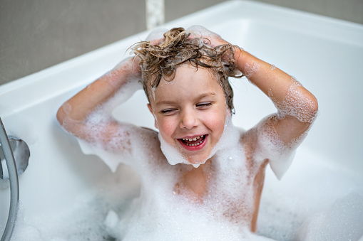 Smiling boy is washing head in bathtub and have fun