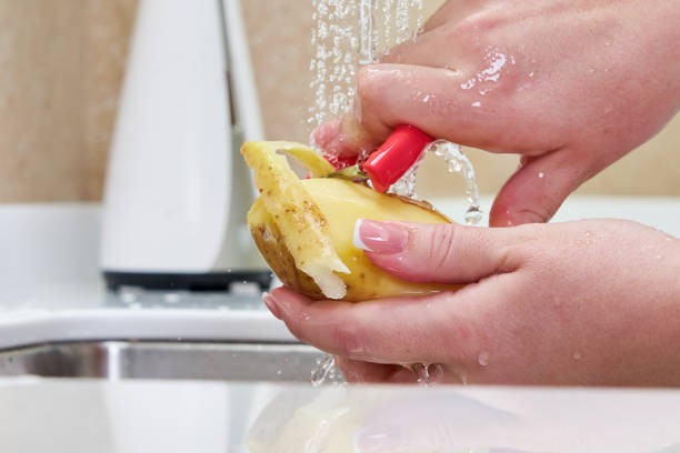 Woman housewife peels potatoes with a knife in the sink over the sink.