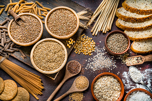 Top view of wholegrain and cereal composition shot on rustic wooden table. This type of food is rich of fiber and is ideal for dieting. The composition includes wholegrain sliced bread, various kinds of wholegrain pasta, wholegrain crackers, grissini, oat flakes, brown rice, spelt and flax seeds. Predominant color is brown. High resolution 42Mp studio digital capture taken with SONY A7rII and Zeiss Batis 40mm F2.0 CF lens