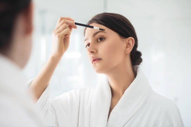 A young woman brushing the eyebrows A reflection in the mirror of a woman brushing her eyebrows in the bathroom lash and brow comb stock pictures, royalty-free photos & images