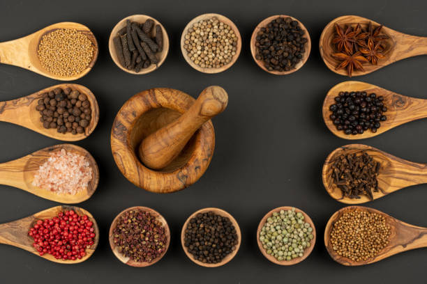 six small wooden bowls and eight cooking spoons made of olive wood filled with various spices and a mortar of olive wood lie on a black background with copy space in the center - mortar and pestle spice seasoning coriander seed imagens e fotografias de stock