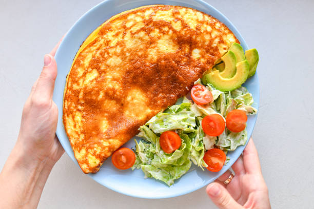 istock fried eggs with vegetables. hands in the frame. Vegetable omelet on a blue plate on a white table, top view 1216804622