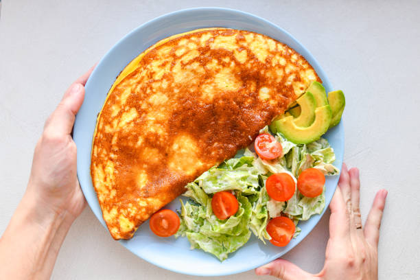 istock fried eggs with vegetables. hands in the frame. Vegetable omelet on a blue plate on a white table, top view 1216804752