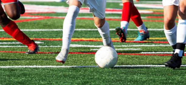 Legs of soccer players chasing ball during game Legs of high school soccer players controlling and chasing the ball during a match on a turf field. high school soccer stock pictures, royalty-free photos & images
