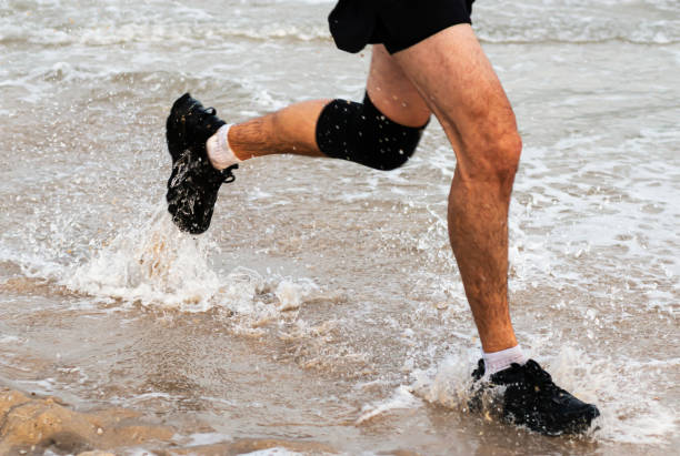 Legs of man running and splashing on edge of beach Runners running a one mile race at the beach splashing in the water as part of the New York State Parks Summer Series of races. knee brace stock pictures, royalty-free photos & images