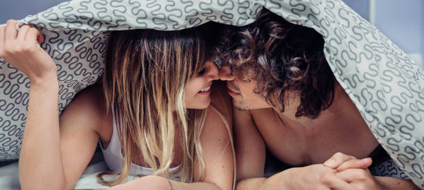 羽毛布団カバーの下でキス愛の幸せな若いカップル - 性的行為 ストックフォトと画像