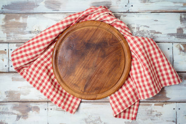 istock Round pizza board with red checked tablecloth on rustic wooden table Kitchen, cooking or baking mock up background for design. Top view from above 1216806388