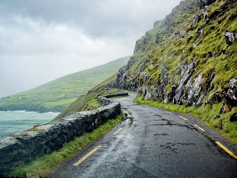 A wet, misty view of a road that follows along the rocky coast of Ireland.