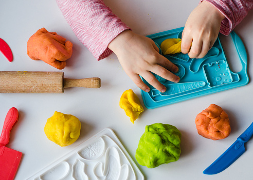 Child's hands with colorful clay. Child playing and creating vagetables from play dough. Girl molding modeling clay. Homemade clay.