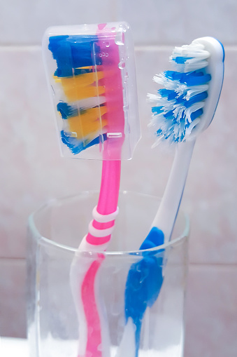 Two toothbrushes in a glass. One toothbrush with protective cap. Dental care and health concept. Portrait capture