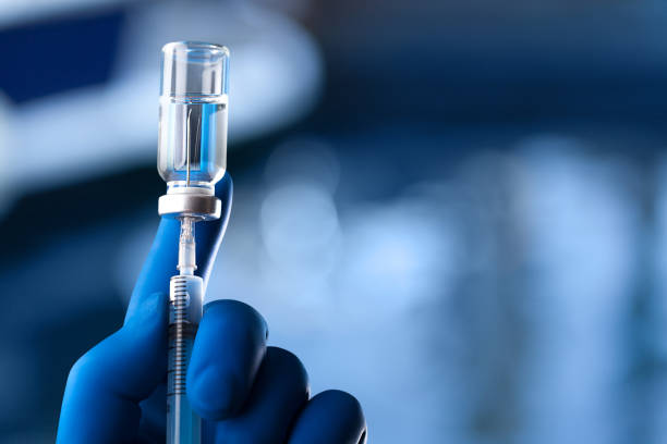 A medical hand in a glove holds an ampoule with a vaccine and a syringe with illustration The hands in blue glove of the scientist hold the processor syringe stock pictures, royalty-free photos & images