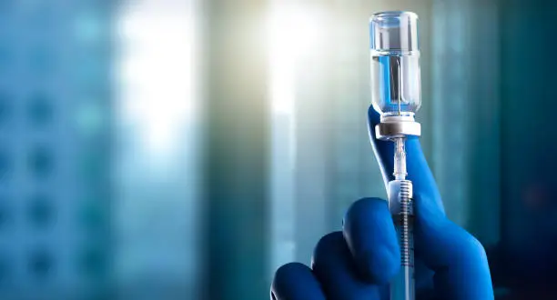 Photo of A medical hand in a glove holds an ampoule with a vaccine and a syringe with illustration