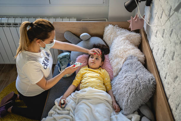 madre con una máscara en la medición de la temperatura de su hija con termómetro digital mientras se acuesta en la cama - offspring child lying on back parent fotografías e imágenes de stock