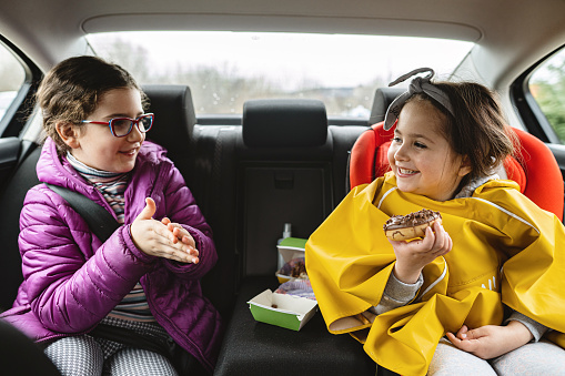 Cheerful 5 year's and 8 year's old sister having a fun on a road trip while eating a chocolate donut