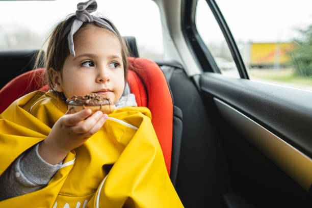 istock Pensive little girl holding chocolate donut while looking through car window 1216815906