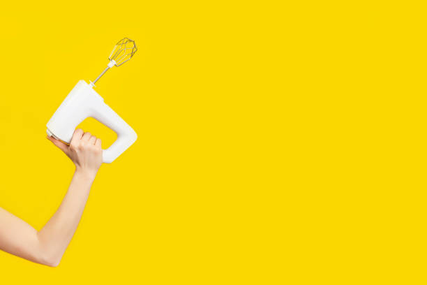 White kitchen mixer in female hand isolated on bright yellow background