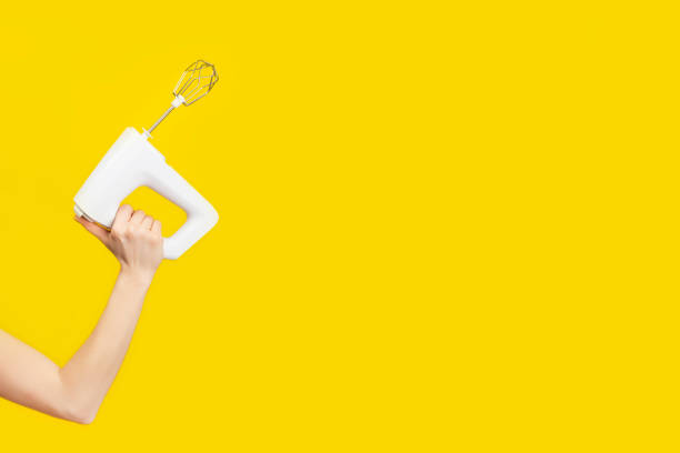 White kitchen mixer in female hand isolated on bright yellow background White kitchen mixer in female hand isolated on bright yellow background. Copy space. Modern kitchen concept electric whisk stock pictures, royalty-free photos & images