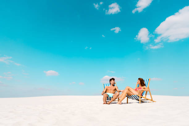 istock smiling young couple sitting in deck chairs on sandy beach 1216817944