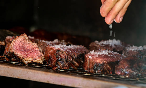 barbecue griglia salando la carne con sale grosso e portandola alla griglia per arrostire - broiling foto e immagini stock