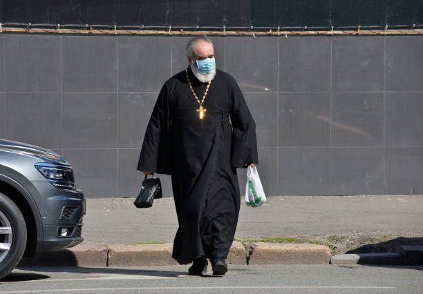 un sacerdote ortodoxo lleva una máscara médica protectora. - sotana fotografías e imágenes de stock