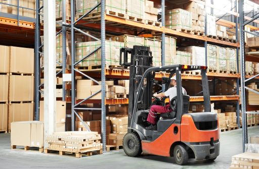 warehouse worker driver in uniform loading cardboxes by forklift stacker loader