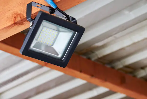 Photo of LED flood light, spot light on the top of the roof. Powerful construction lighting floodlight a lantern for illumination of a local area at night