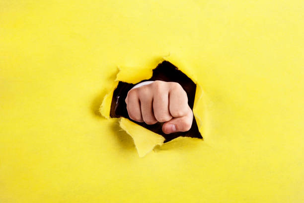 istock Fist punching through a ripped hole in a paper 1216821001