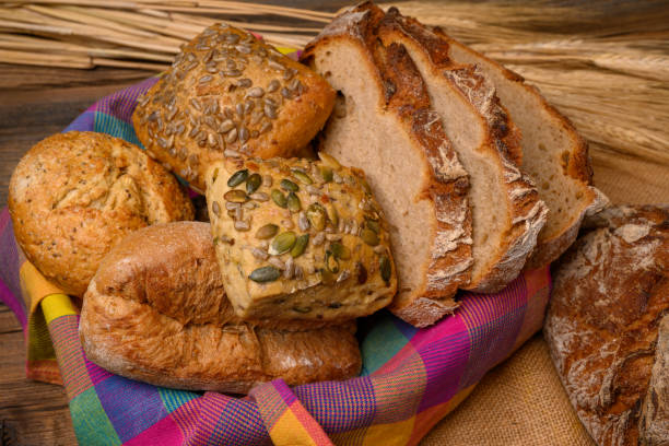 istock Freshly various buns and bread slices in a basket and a half whole grain bread on a jute fabric placed on a rustic wooden background with grain ears. 1216822367