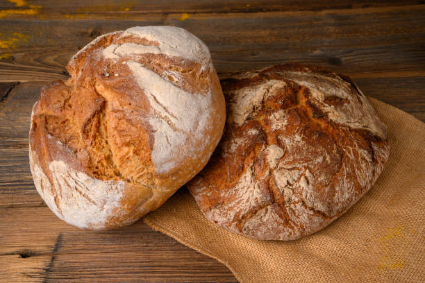istock Two fresh whole grain breads from the baker on a jute fabric on a rustic wooden background. 1216822695